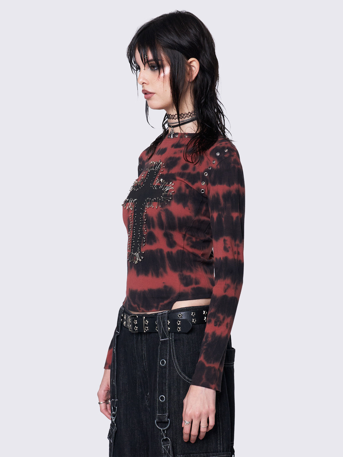 Asymmetric long sleeve top with black and red tie-dye pattern, cross patch with safety pins, silver eyelets at neckline and armhole, slim fit.