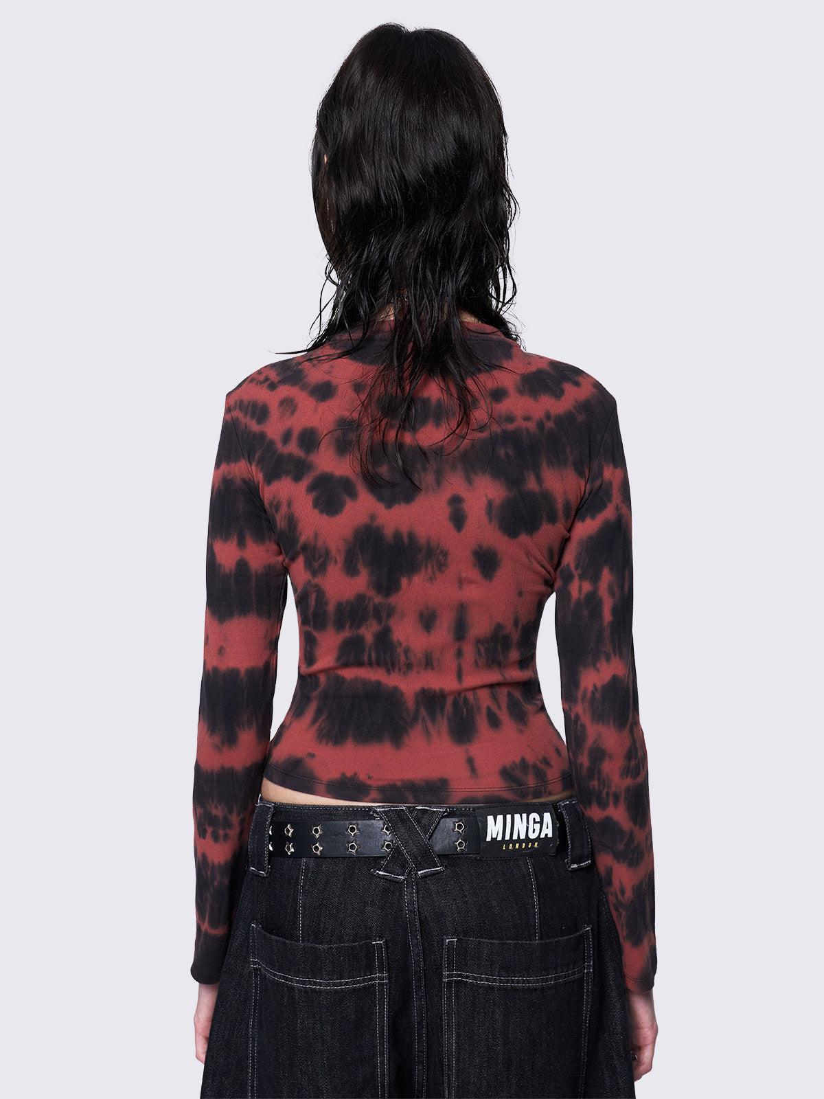 Asymmetric long sleeve top with black and red tie-dye pattern, cross patch with safety pins, silver eyelets at neckline and armhole, slim fit.