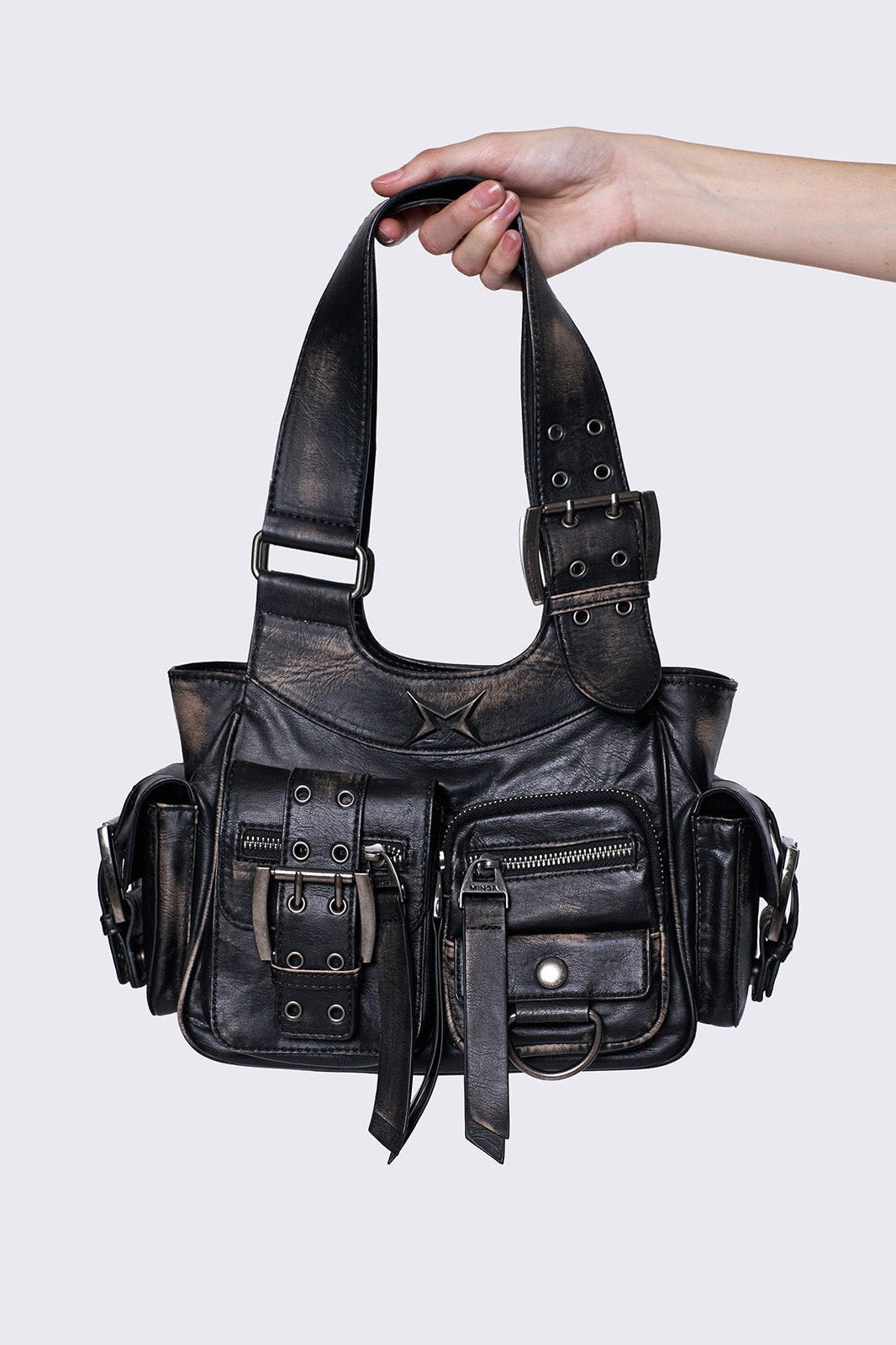 Black leather handbag with multiple pockets, buckles, and a star design, held by a hand, featuring an edgy, utilitarian style.
