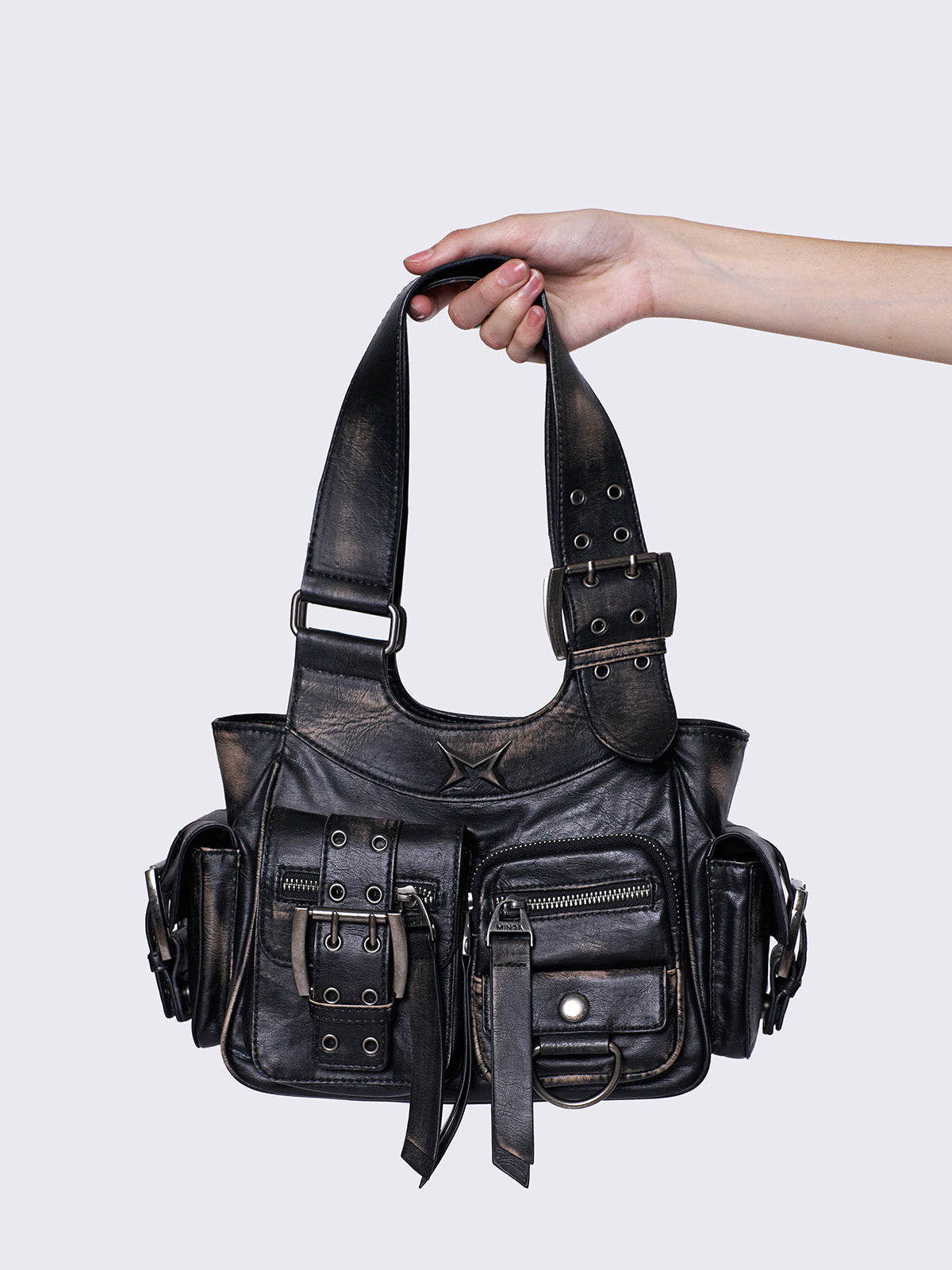 Black leather handbag with multiple pockets, buckles, and a star design, held by a hand, featuring an edgy, utilitarian style.