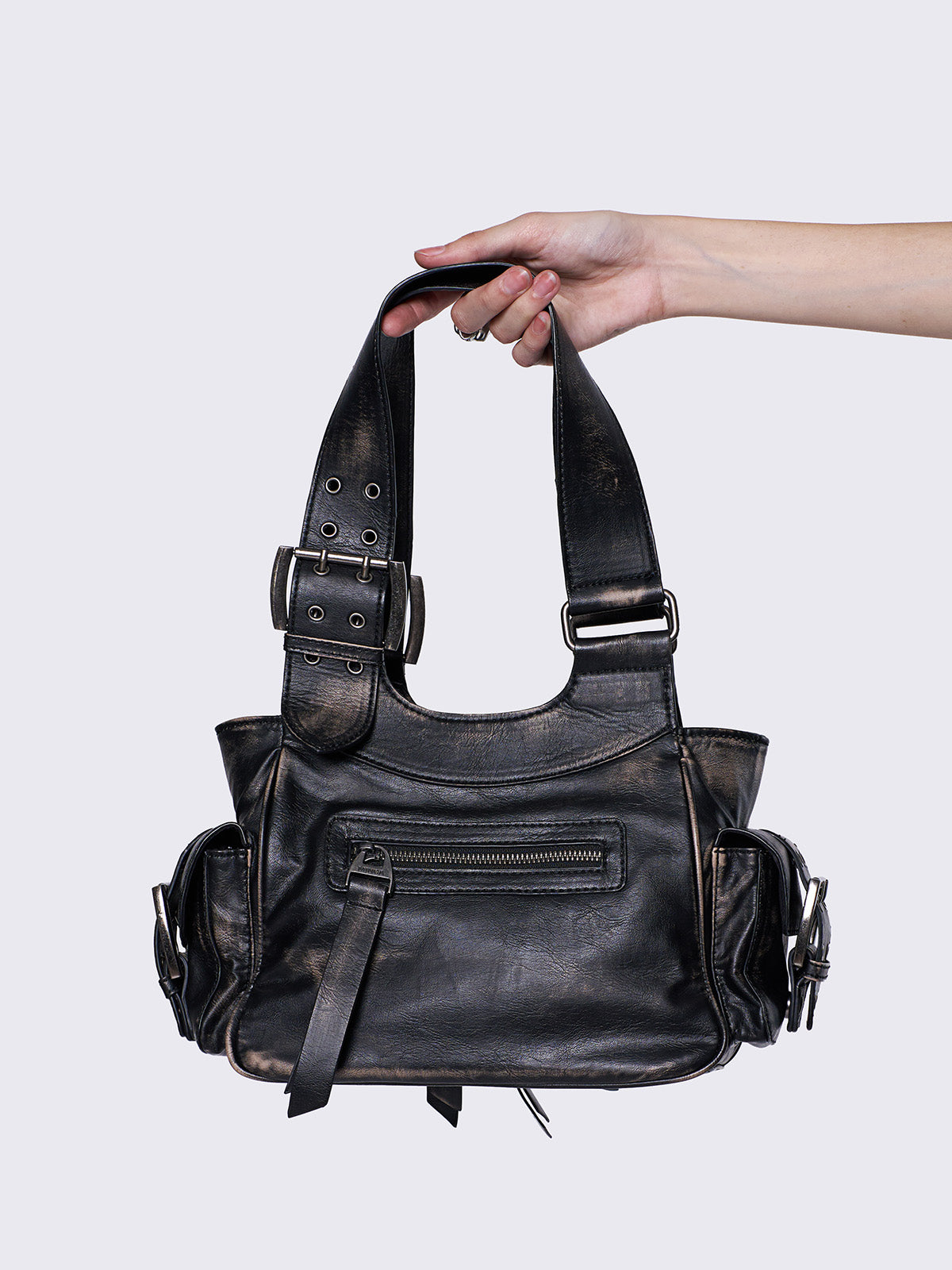 Black leather handbag with multiple pockets, buckles, and a star design, held by a hand, featuring an edgy, utilitarian style.