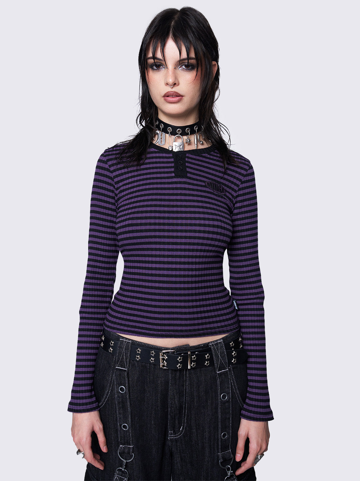 Slim-fit ribbed top with purple and black stripes, half button placket, Minga embroidered logo, and rounded neckline. Y2K and grunge-inspired style