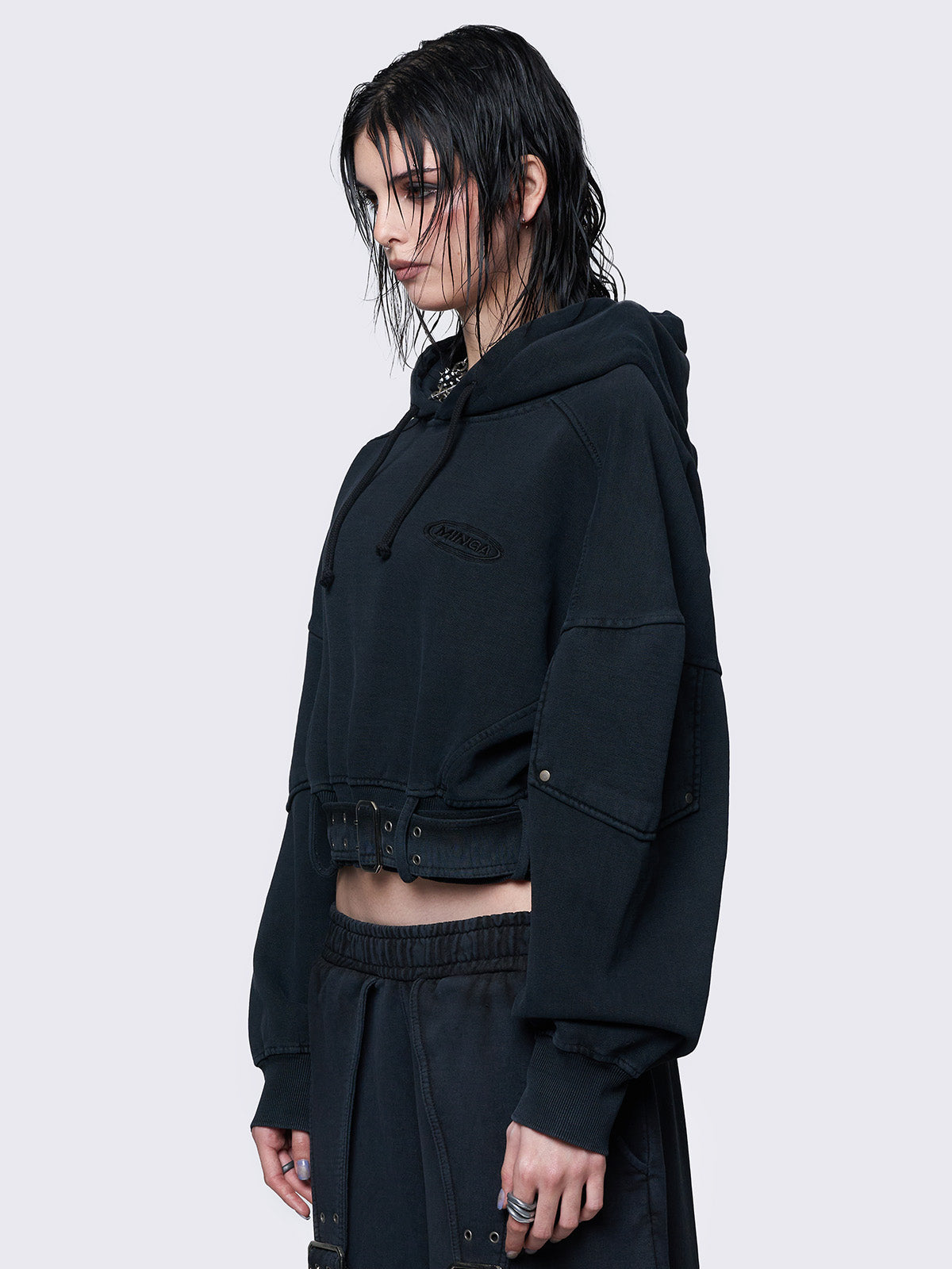 Cropped washed black hoodie with a detachable buckle belt at the hem, an embroidered logo on the chest, raglan sleeves, and a drawstring hood. Stylish and comfortable.