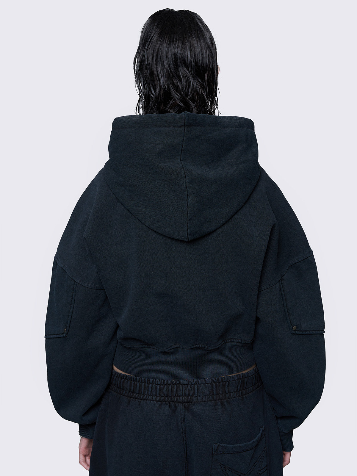 Cropped washed black hoodie with a detachable buckle belt at the hem, an embroidered logo on the chest, raglan sleeves, and a drawstring hood. Stylish and comfortable.