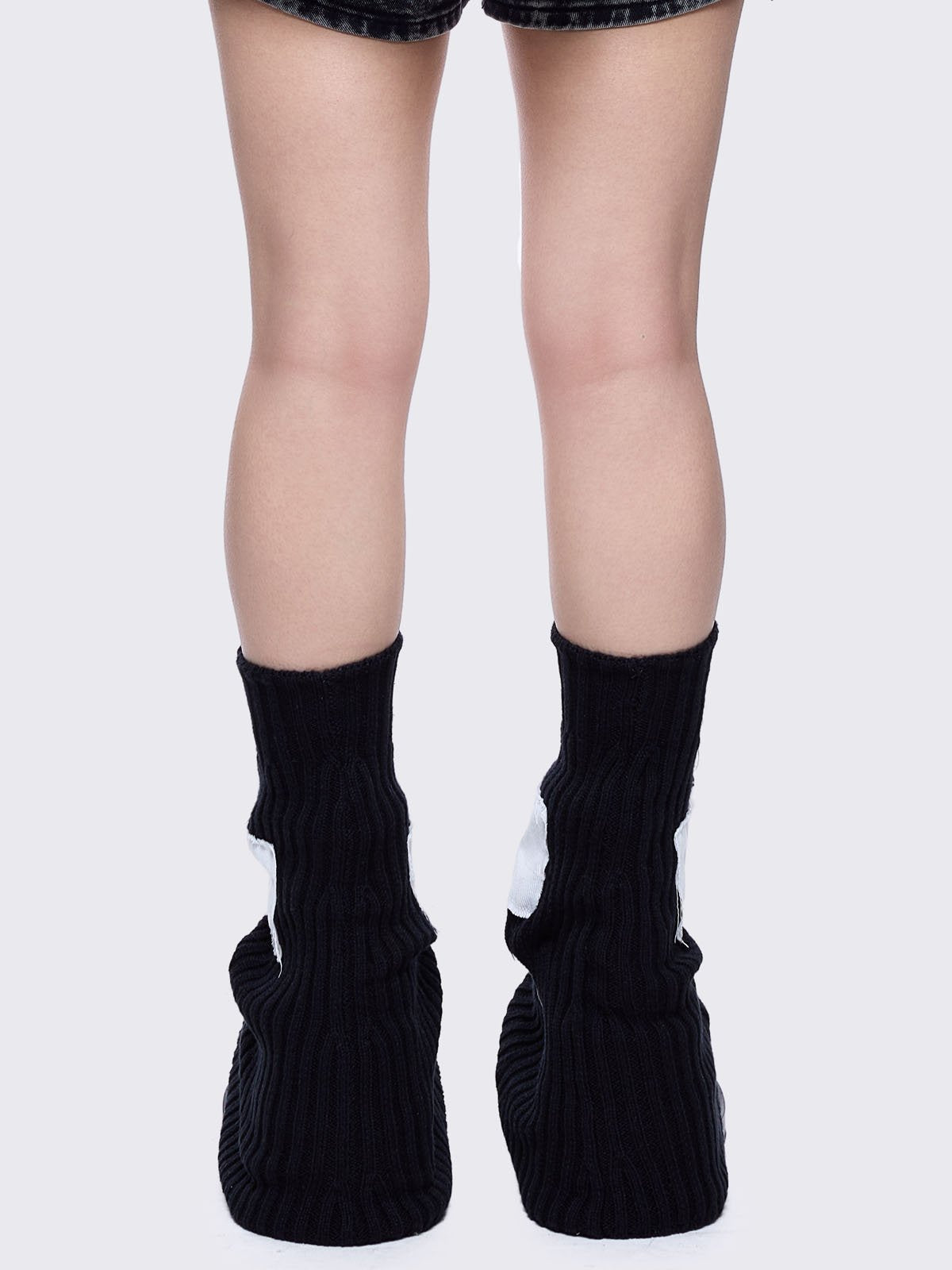 Black knitted flare leg warmers featuring a white chunky cross patch 