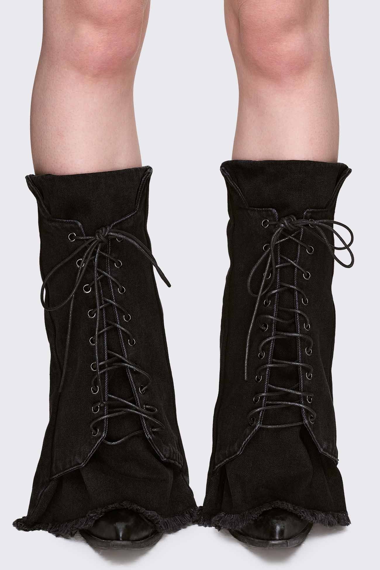 Black denim leg warmer with front lace-up detail, flared shape and raw frayed hem in a grunge Y2K style.