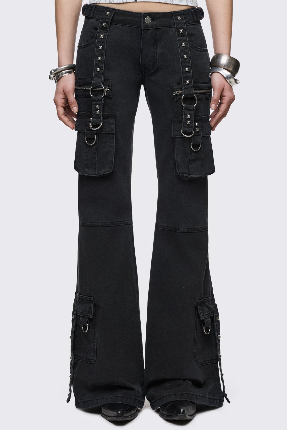 Black cotton cargo jeans with flared leg, studded straps, zip pockets and D-ring details in a goth Y2K style.