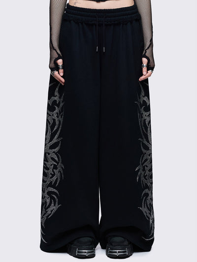 Loose-fit wide-leg sweatpants featuring a large, detailed tribal sigil pattern made of silver rhinestones running down the side seam.