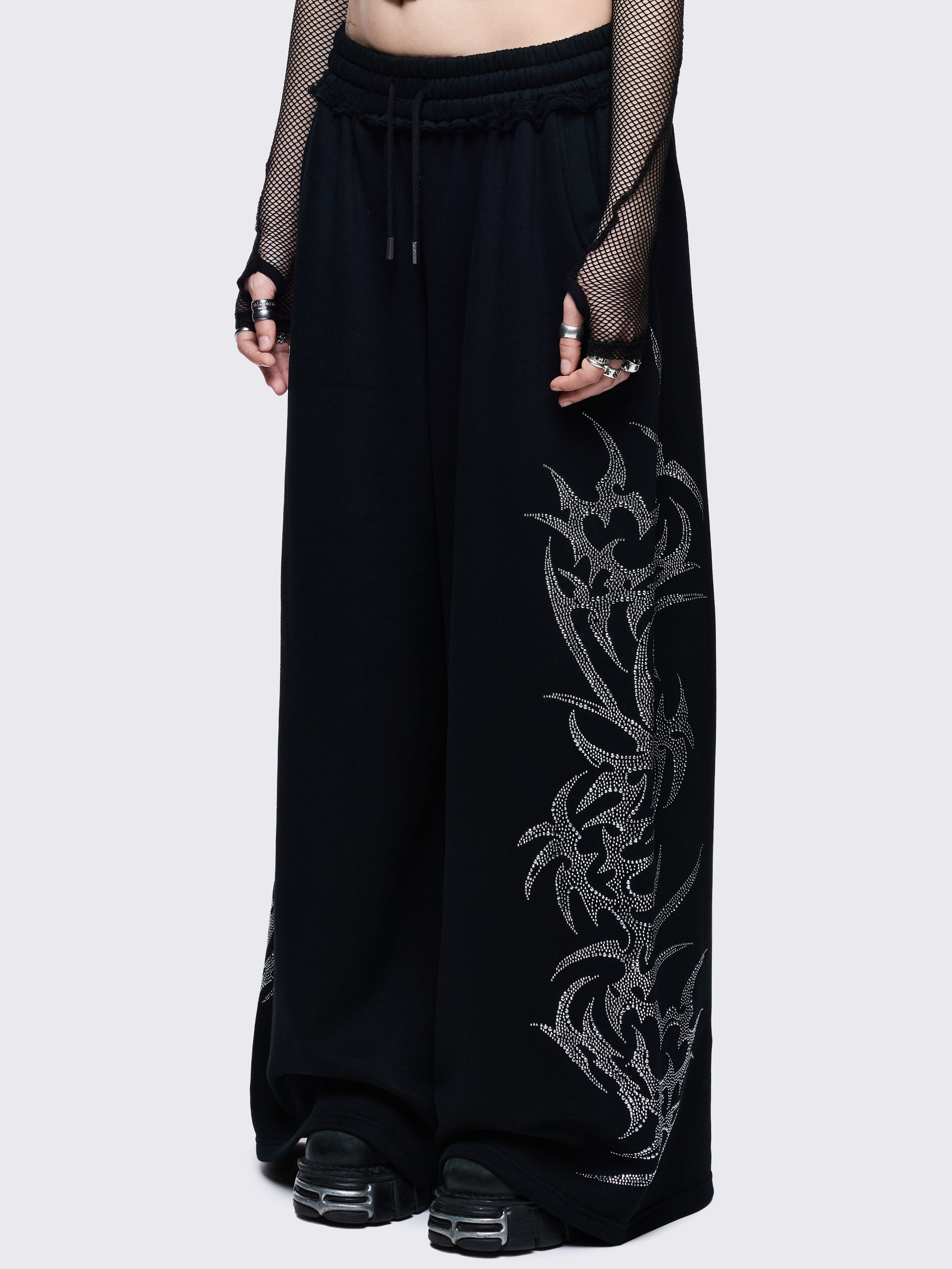 Loose-fit wide-leg sweatpants featuring a large, detailed tribal sigil pattern made of silver rhinestones running down the side seam.