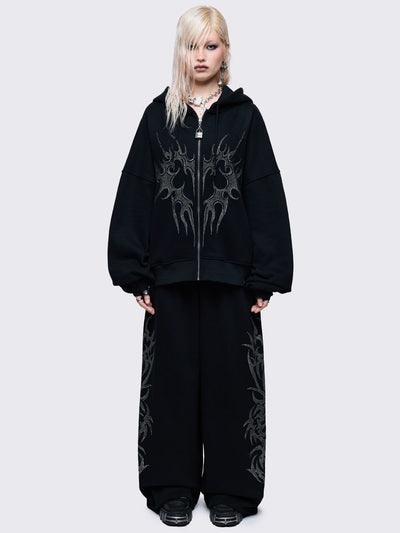Loose-fit wide-leg sweatpants featuring a large, detailed tribal sigil pattern made of silver rhinestones running down the side seam.