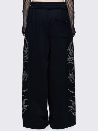 Loose-fit wide-leg sweatpants featuring a large, detailed tribal sigil pattern made of silver rhinestones running down the side seam.