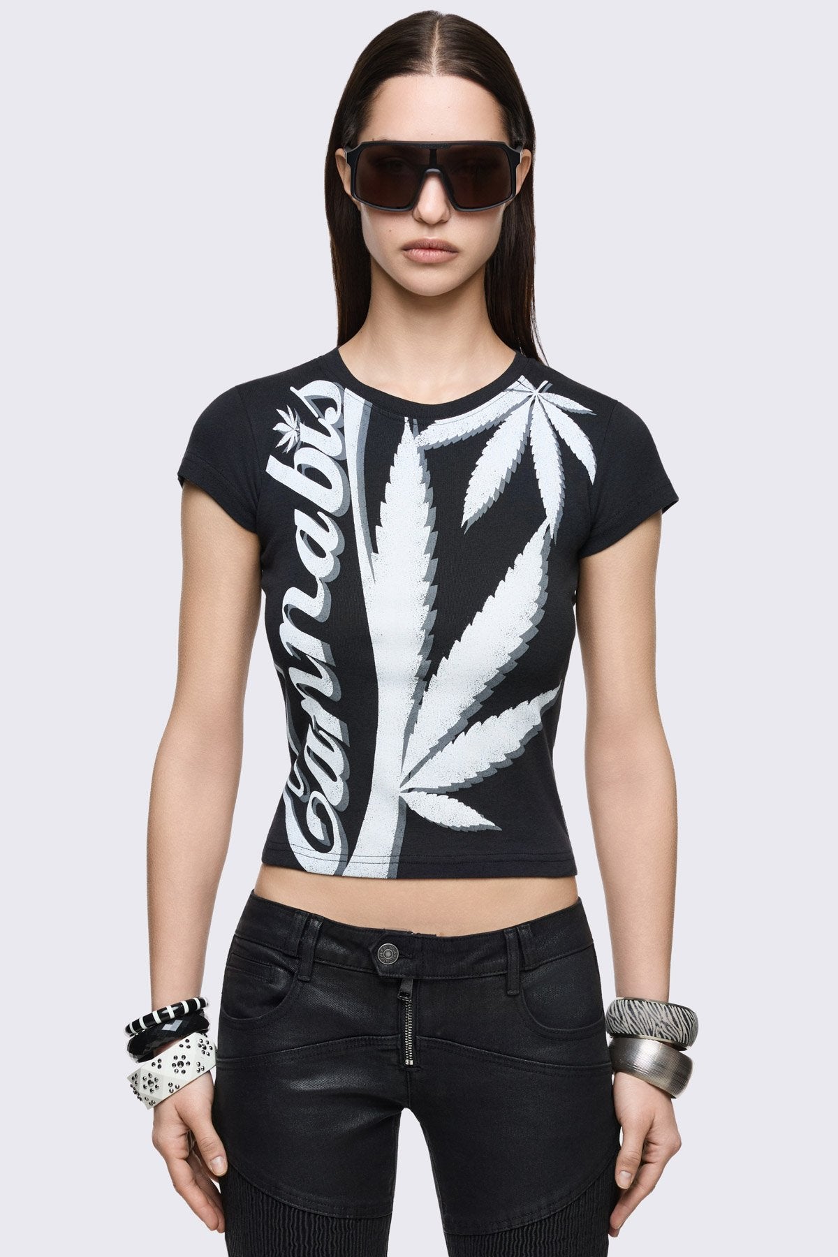 Black cotton baby tee with bold cannabis leaf graphic and logo print, fitted grunge style.
