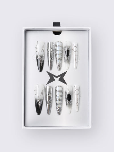 Press-on nail set in chrome and white with marble, piercing rings, chain lacing, and stiletto shape for a grunge glam look.