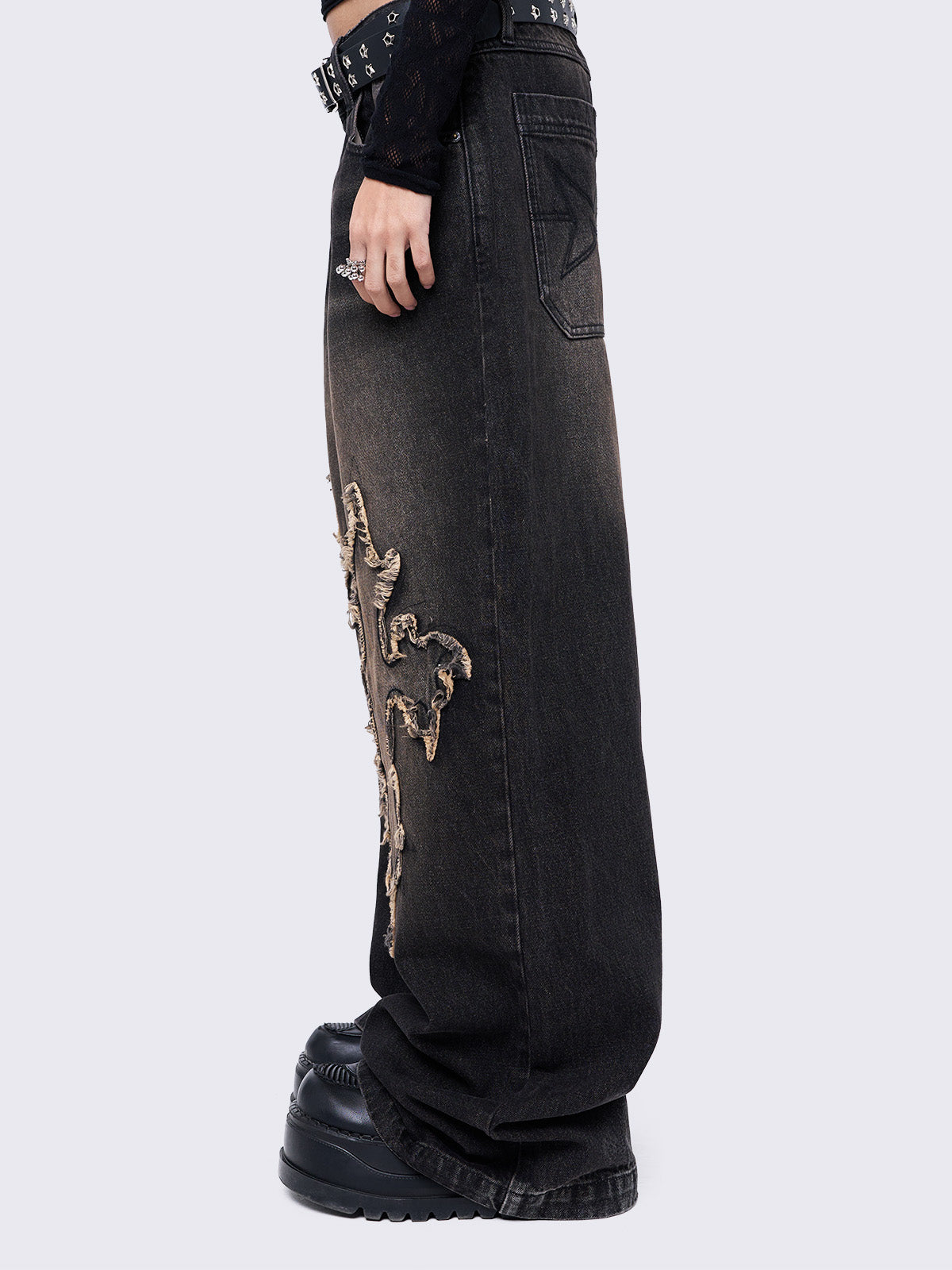 Black washed baggy jeans with brown overdye featuring a cross raw edge patches.