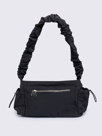 Black shoulder bag with ruched strap, lace-up ribbon front pockets, detachable plush pink bunny charm, and multiple pockets.