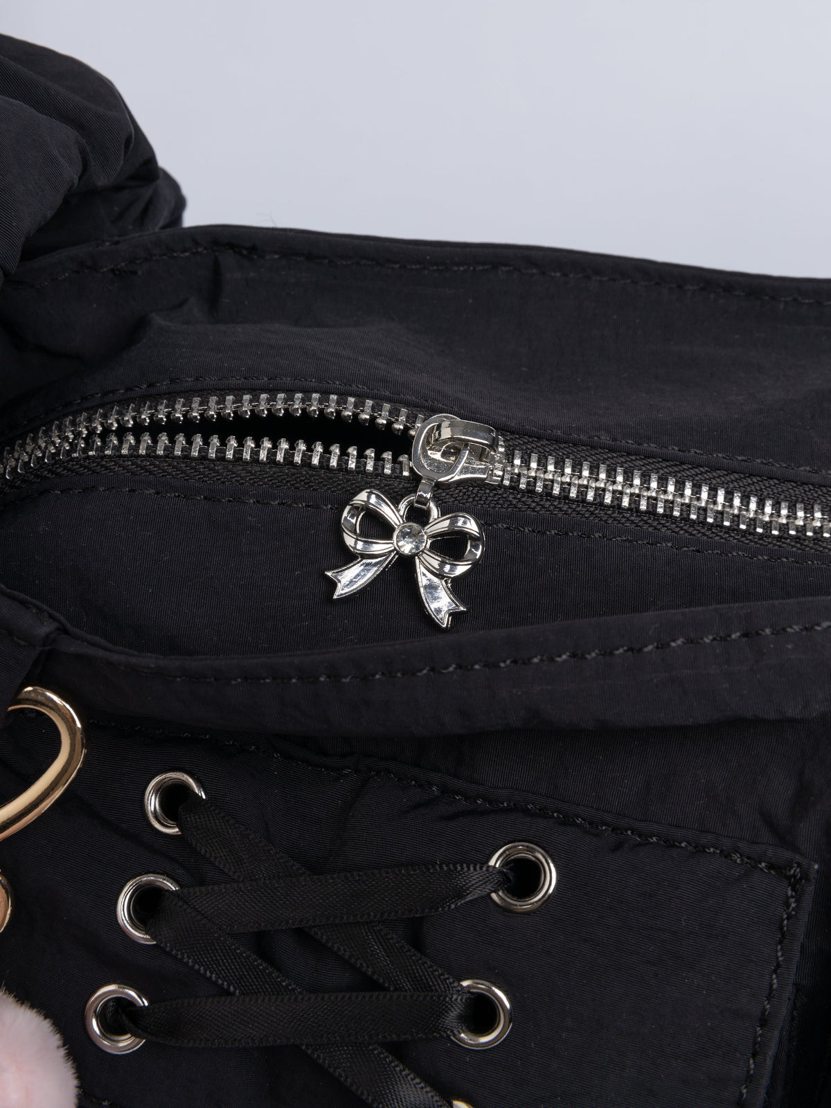 Black shoulder bag with ruched strap, lace-up ribbon front pockets, detachable plush pink bunny charm, and multiple pockets.