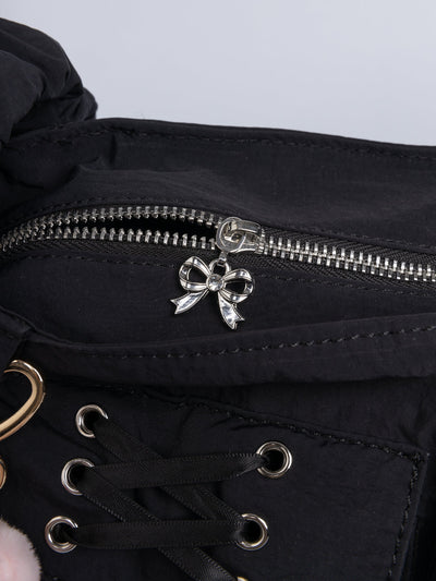 Black shoulder bag with ruched strap, lace-up ribbon front pockets, detachable plush pink bunny charm, and multiple pockets.
