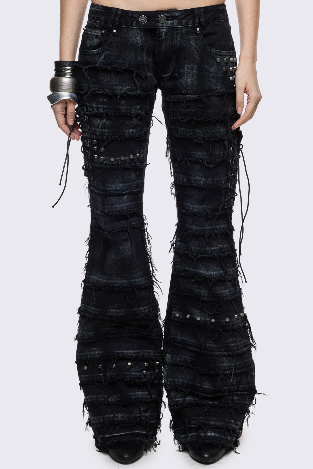 Black washed denim flare jeans with distressed panels, stud and lace-up details in a grunge Y2K style.