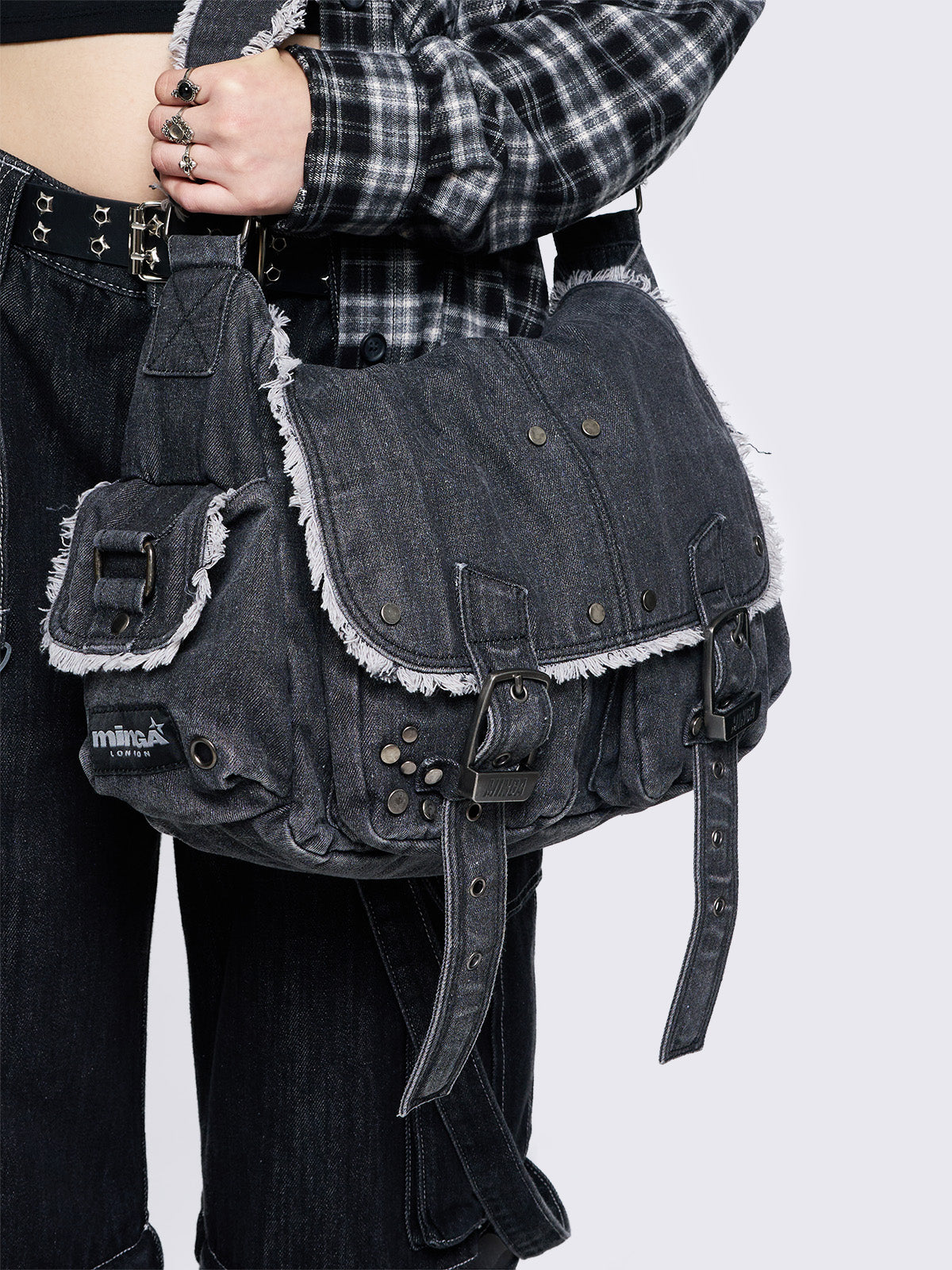 Black wash denim shoulder bag with frayed edges, flap closure, buckle straps, and studded details. Perfect for grunge and Y2K-inspired streetwear.