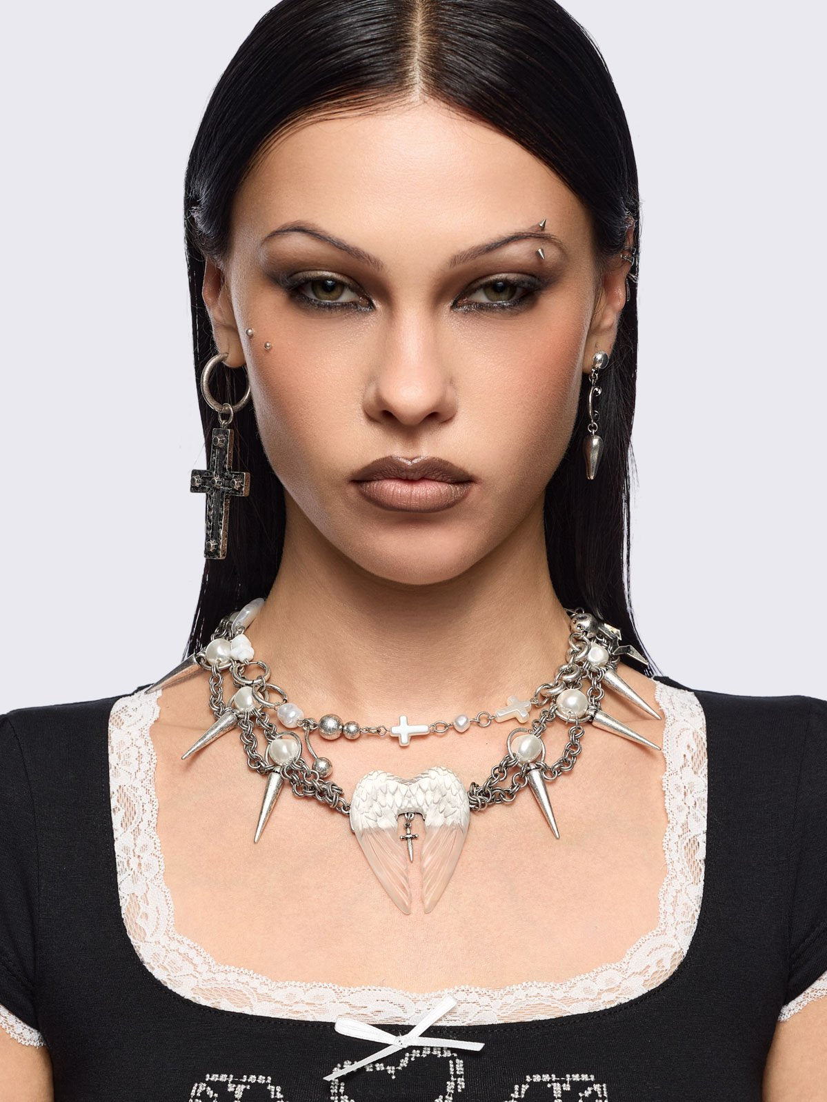 Chunky silver charm necklace with spike, pearl, piercing and cross details and a chunky angel wings pendant.