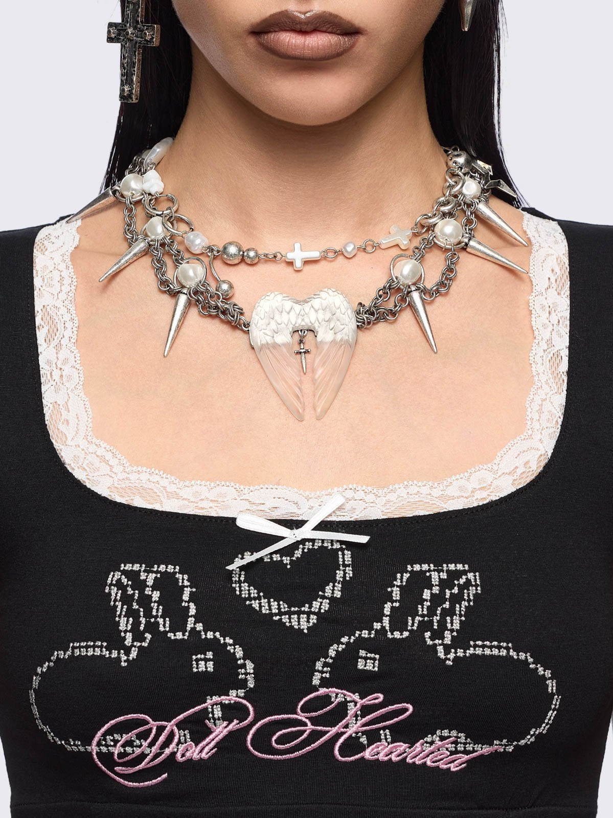 Chunky silver charm necklace with spike, pearl, piercing and cross details and a chunky angel wings pendant.