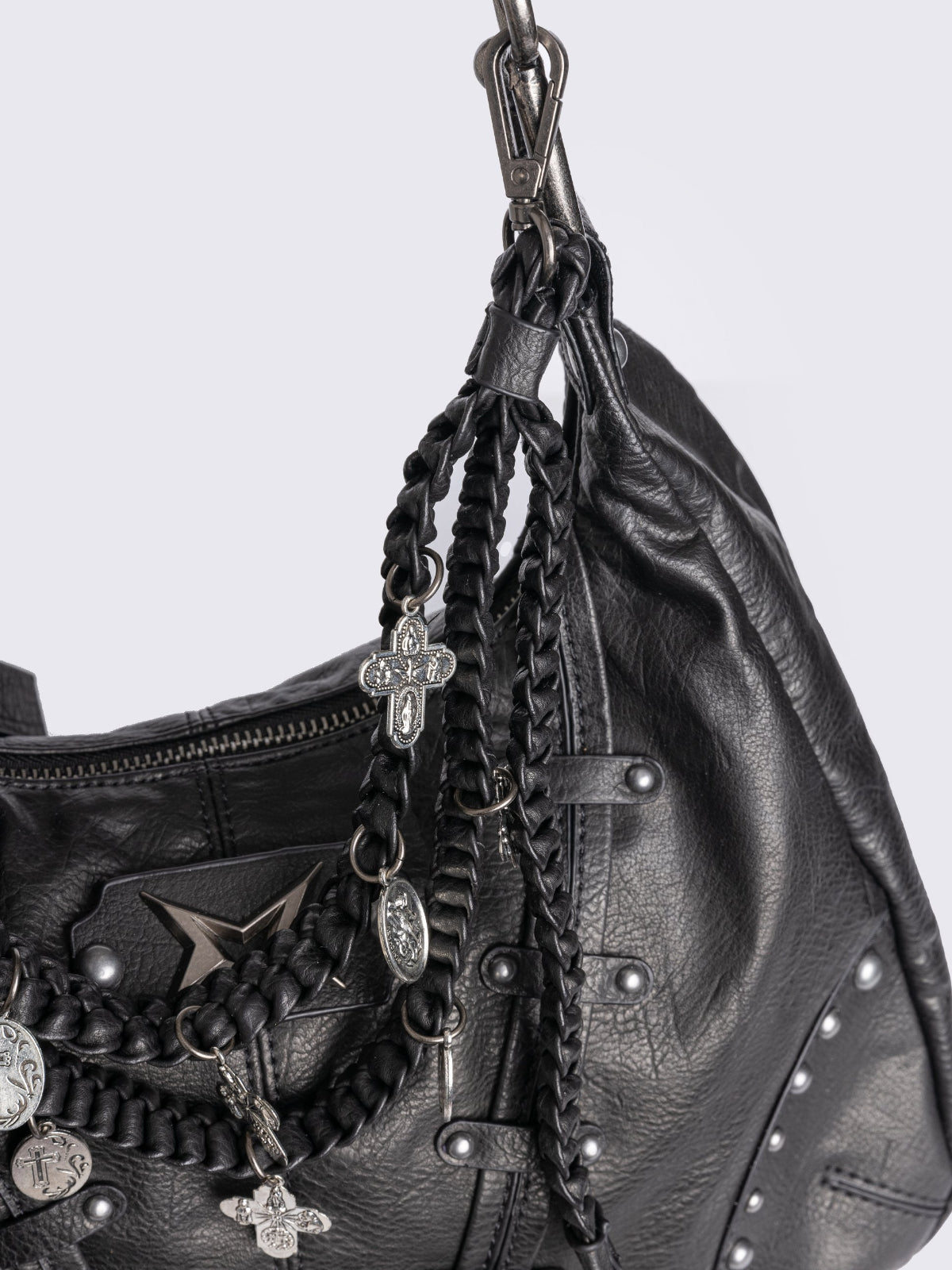 A black leather hobo bag decorated with silver studs, metallic charms, braided leather, and a large grey and white fur tail charm.