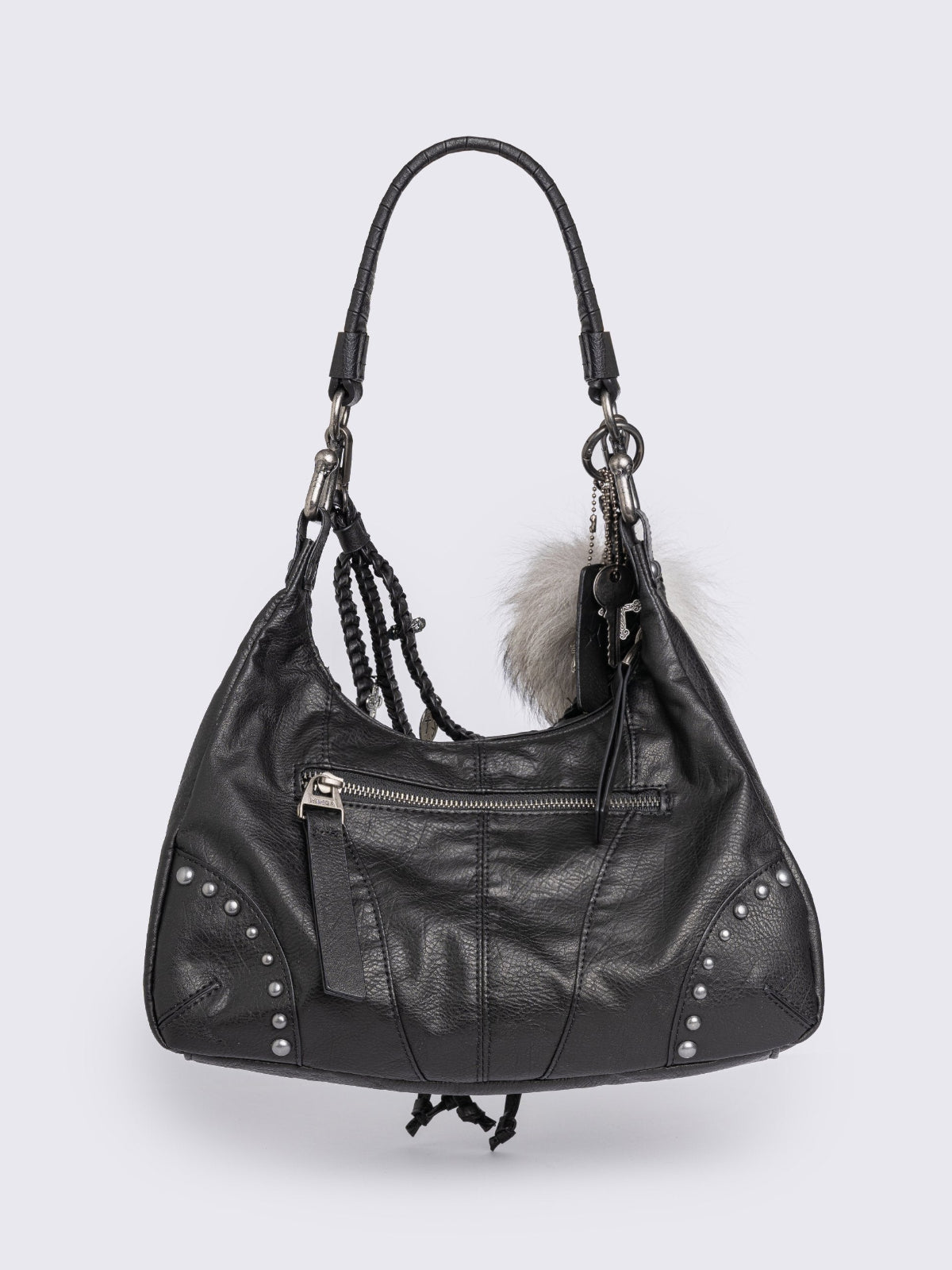 A black leather hobo bag decorated with silver studs, metallic charms, braided leather, and a large grey and white fur tail charm.