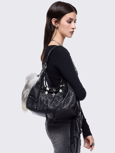 A black leather hobo bag decorated with silver studs, metallic charms, braided leather, and a large grey and white fur tail charm.