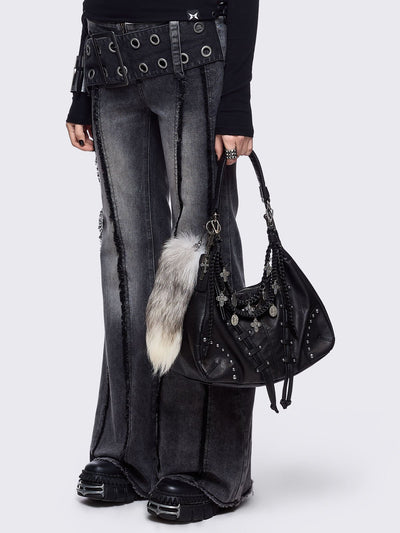 A black leather hobo bag decorated with silver studs, metallic charms, braided leather, and a large grey and white fur tail charm.
