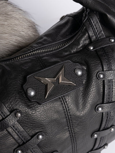 A black leather hobo bag decorated with silver studs, metallic charms, braided leather, and a large grey and white fur tail charm.