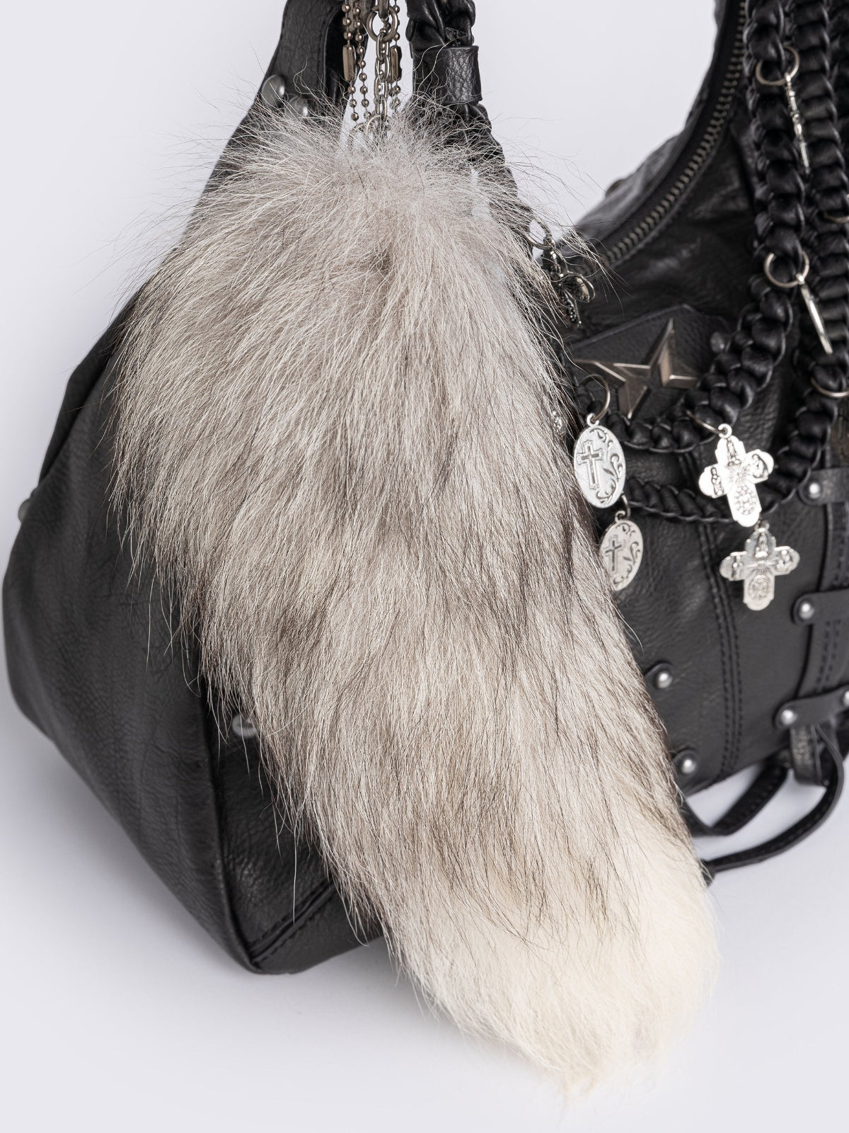 A black leather hobo bag decorated with silver studs, metallic charms, braided leather, and a large grey and white fur tail charm.