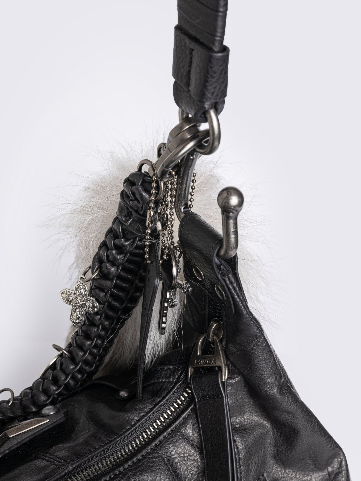A black leather hobo bag decorated with silver studs, metallic charms, braided leather, and a large grey and white fur tail charm.