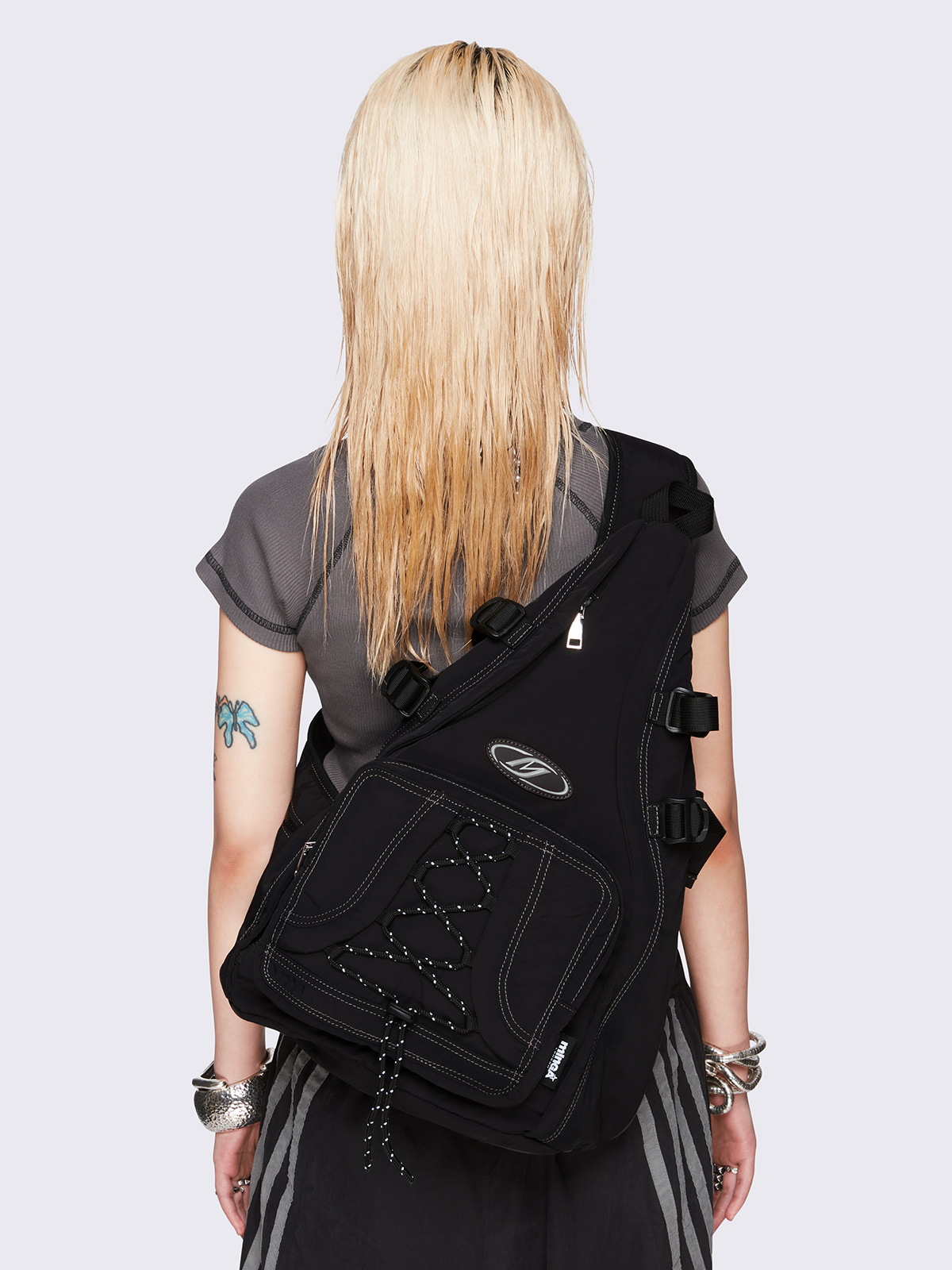 Black nylon sling bag featuring contrast stitching, multiple zip pockets and front bungee-cord detail.