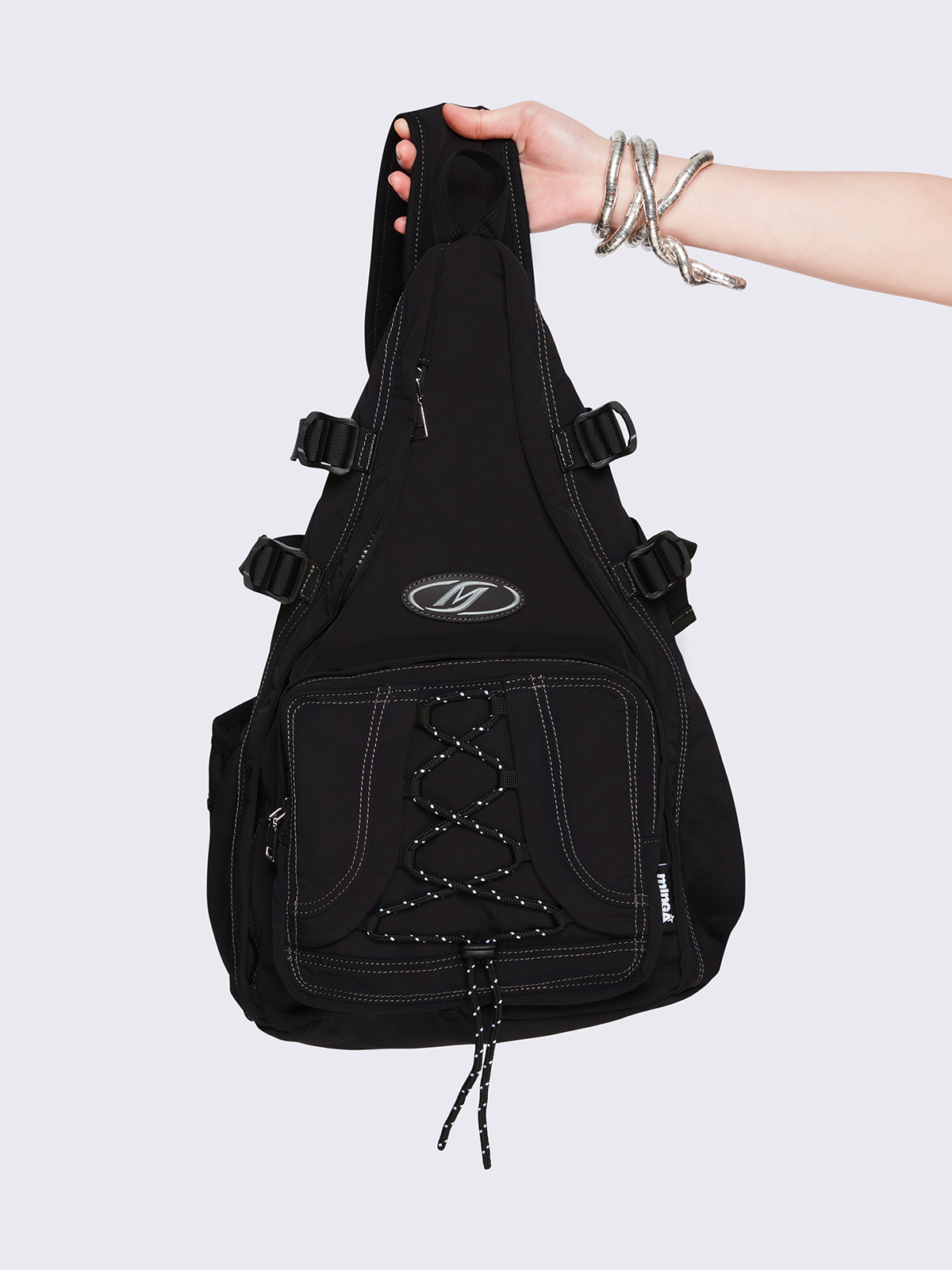 Black nylon sling bag featuring contrast stitching, multiple zip pockets and front bungee-cord detail.