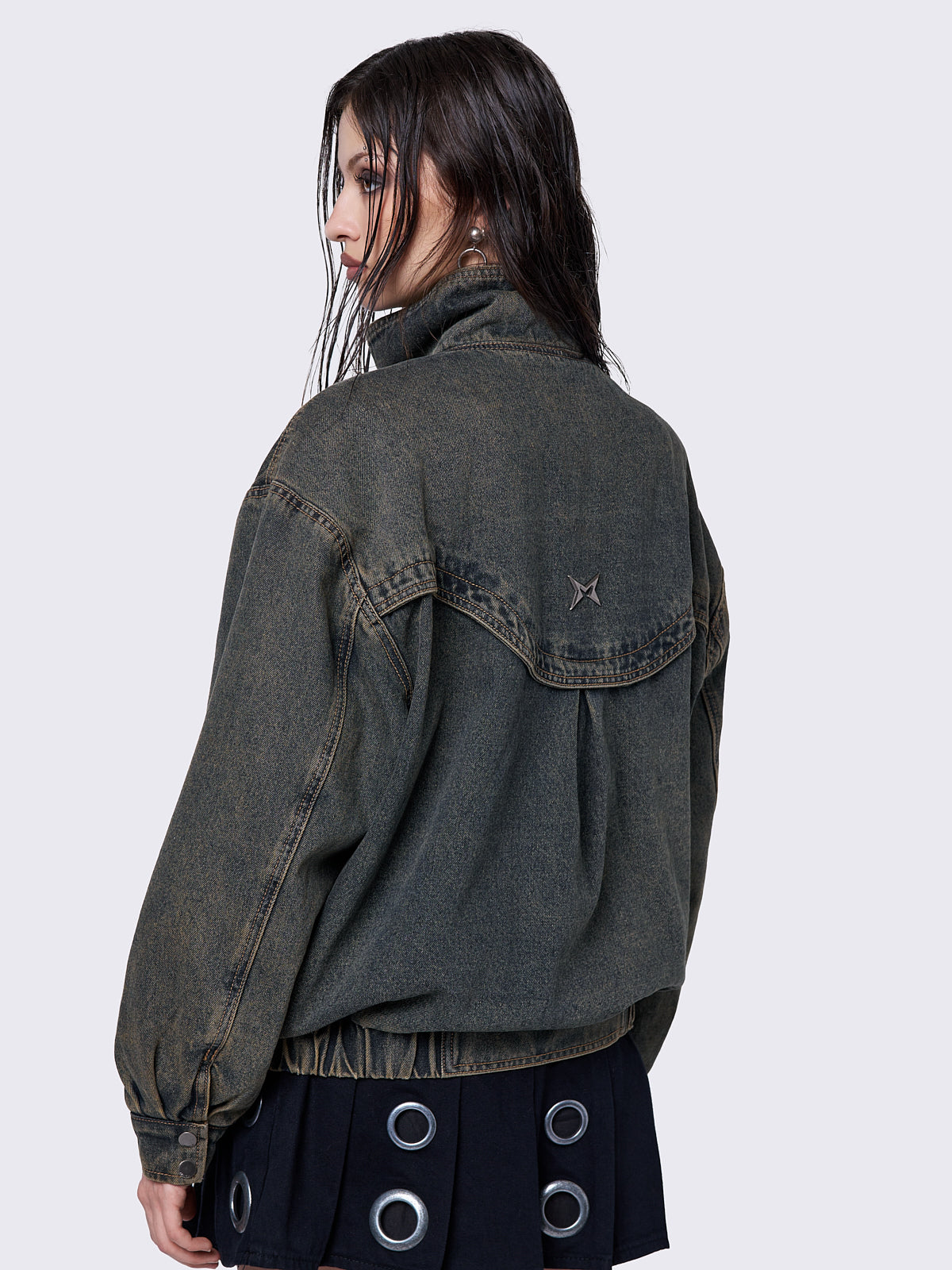 Blue washed denim bomber jacket with a brown overdye finish. The jacket features a boxy, oversized fit and a high crossover collar neck. It has multiple pockets and a Minga logo metal detail for added style.