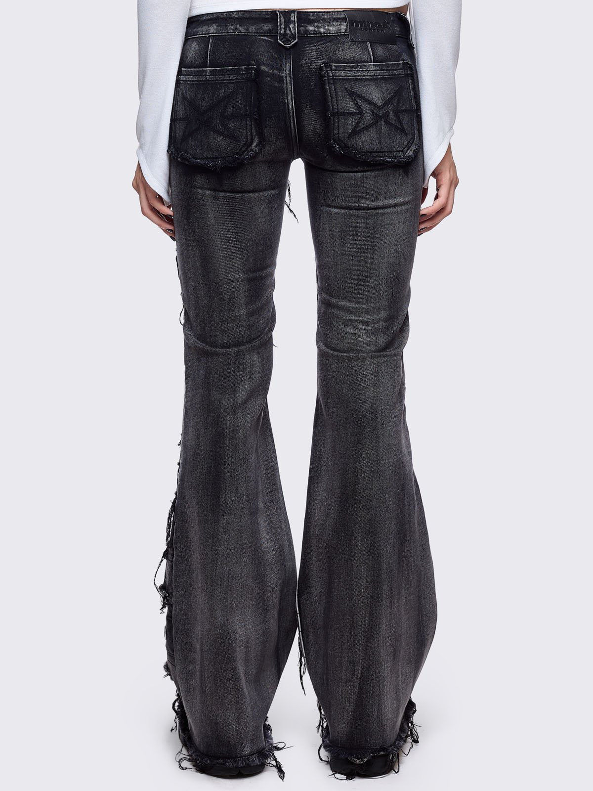 Black washed flare jeans featuring heavy distressed and shedded, eyelet, piercing and stud details. 
