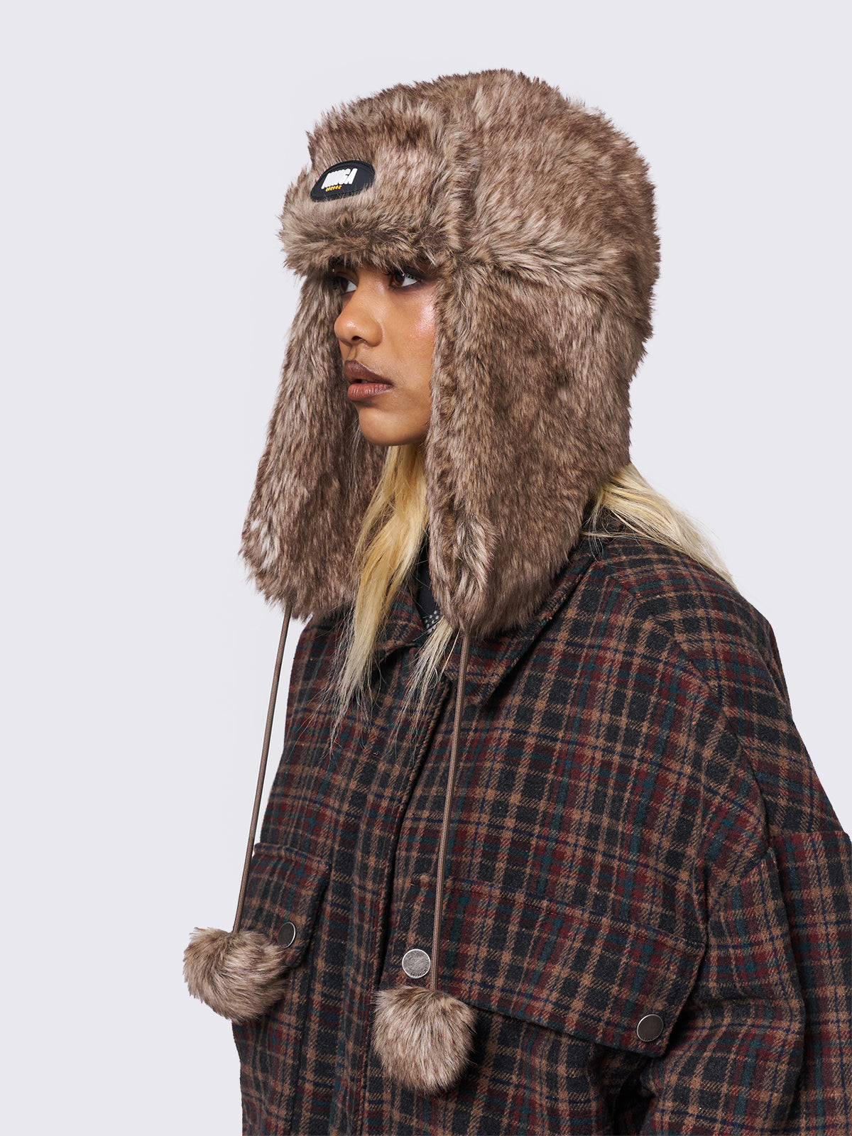 Faux fur trapper hat in brown with minga rubber logo detail and ear flaps