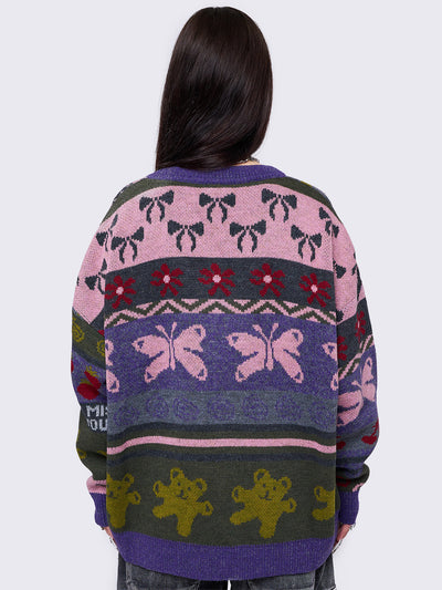 Purple jacquard knit cardigan with playful motifs including teddy bear, bows, flowers and geometric striped pattern.