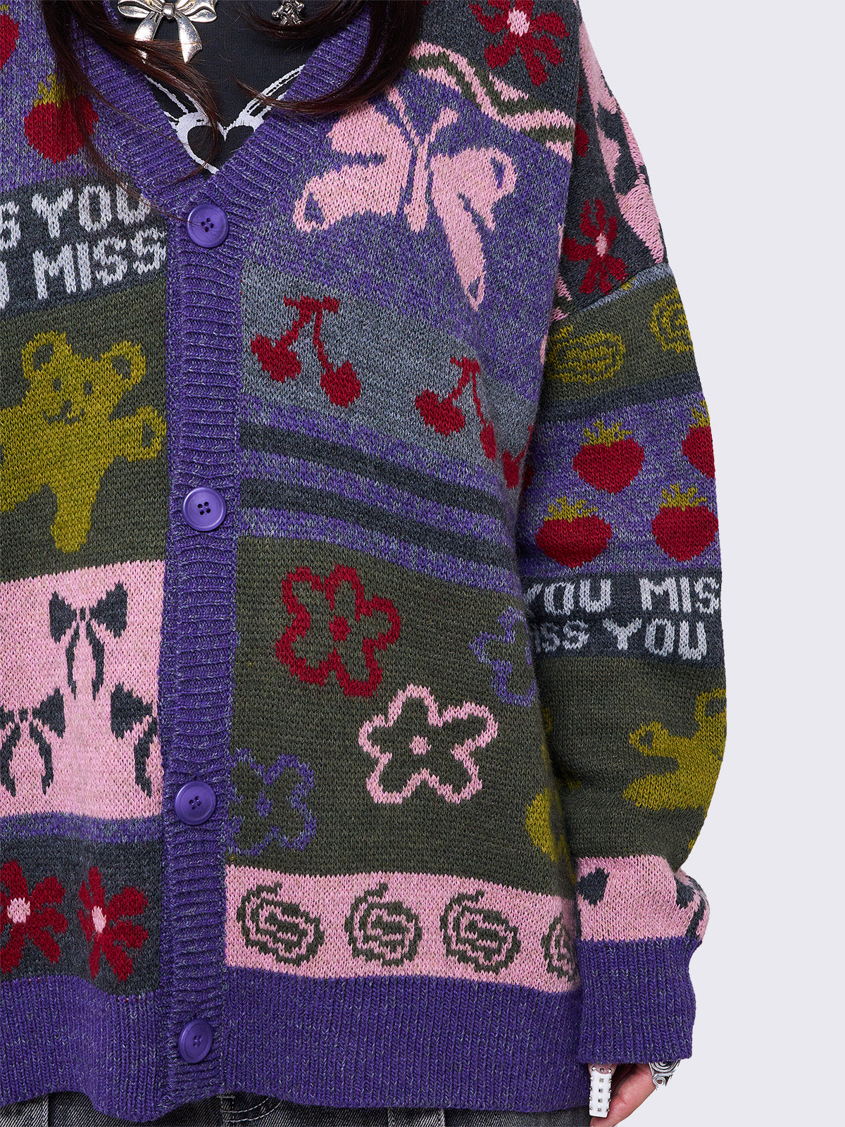 Purple jacquard knit cardigan with playful motifs including teddy bear, bows, flowers and geometric striped pattern.