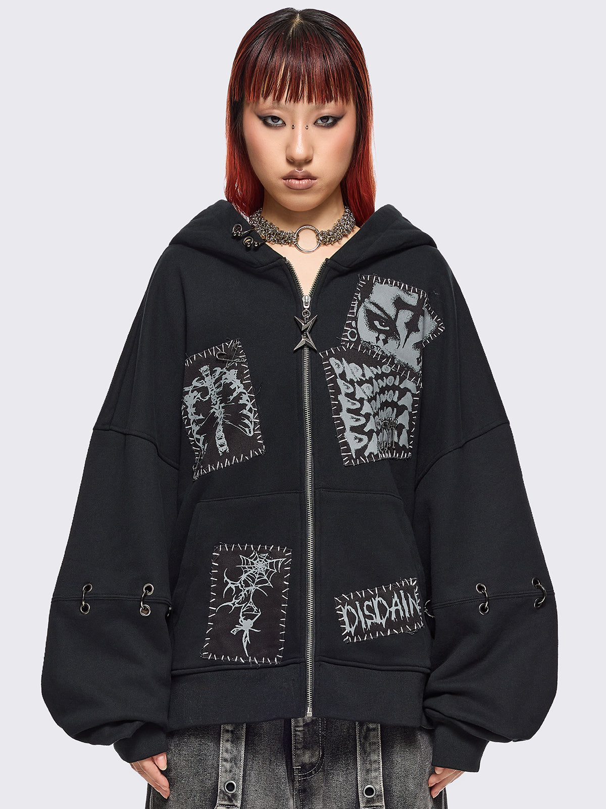 Black zip up hoodie jacket with white grunge print patches and eyelets with O-ring and piercing details.