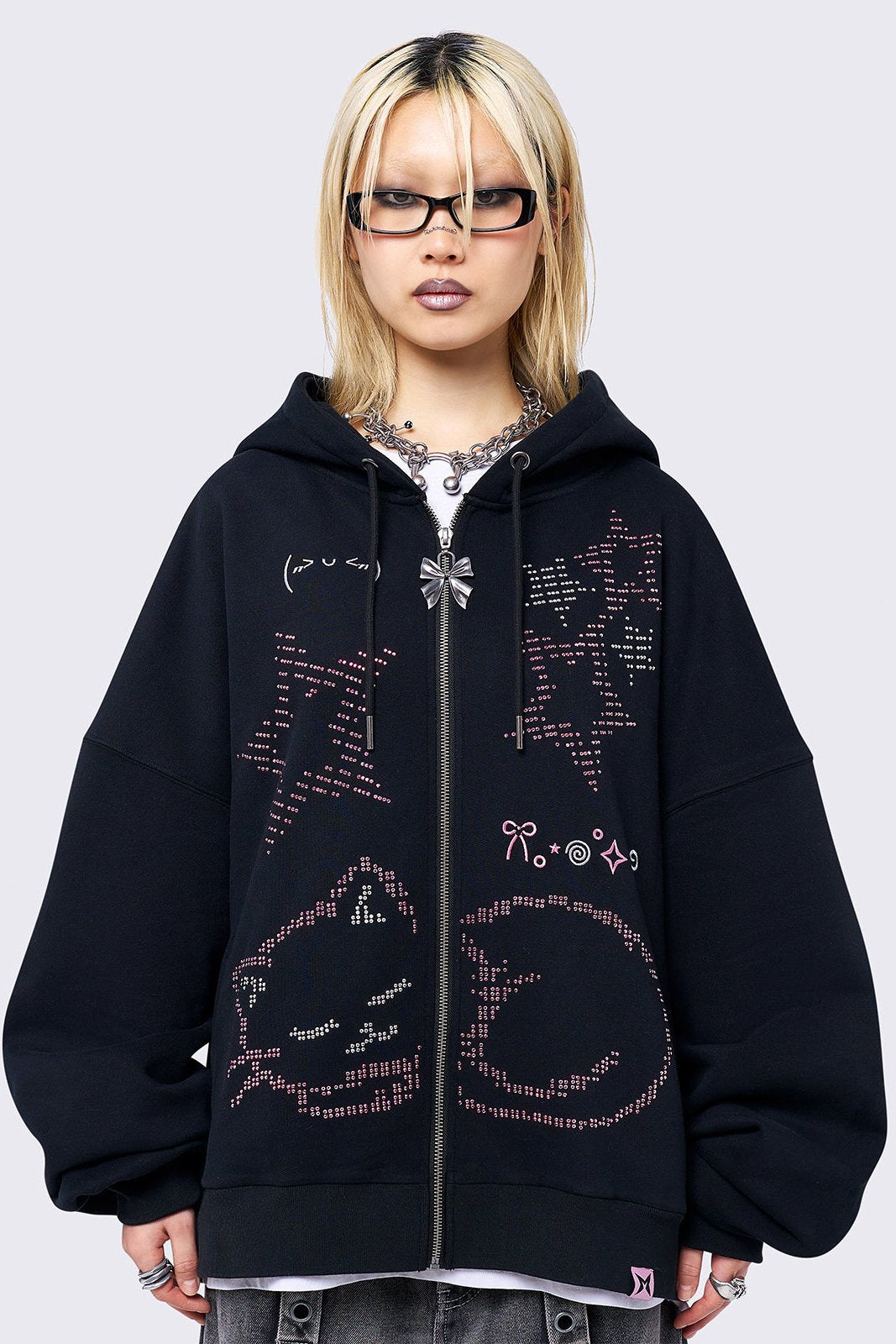 Black zip-up hoodie jacket featuring a pink cat and stars graphic with stud and embroidery details. Designed with a drawstring hood, zip fastening, long sleeves, ribbed trims, and an oversized fit.