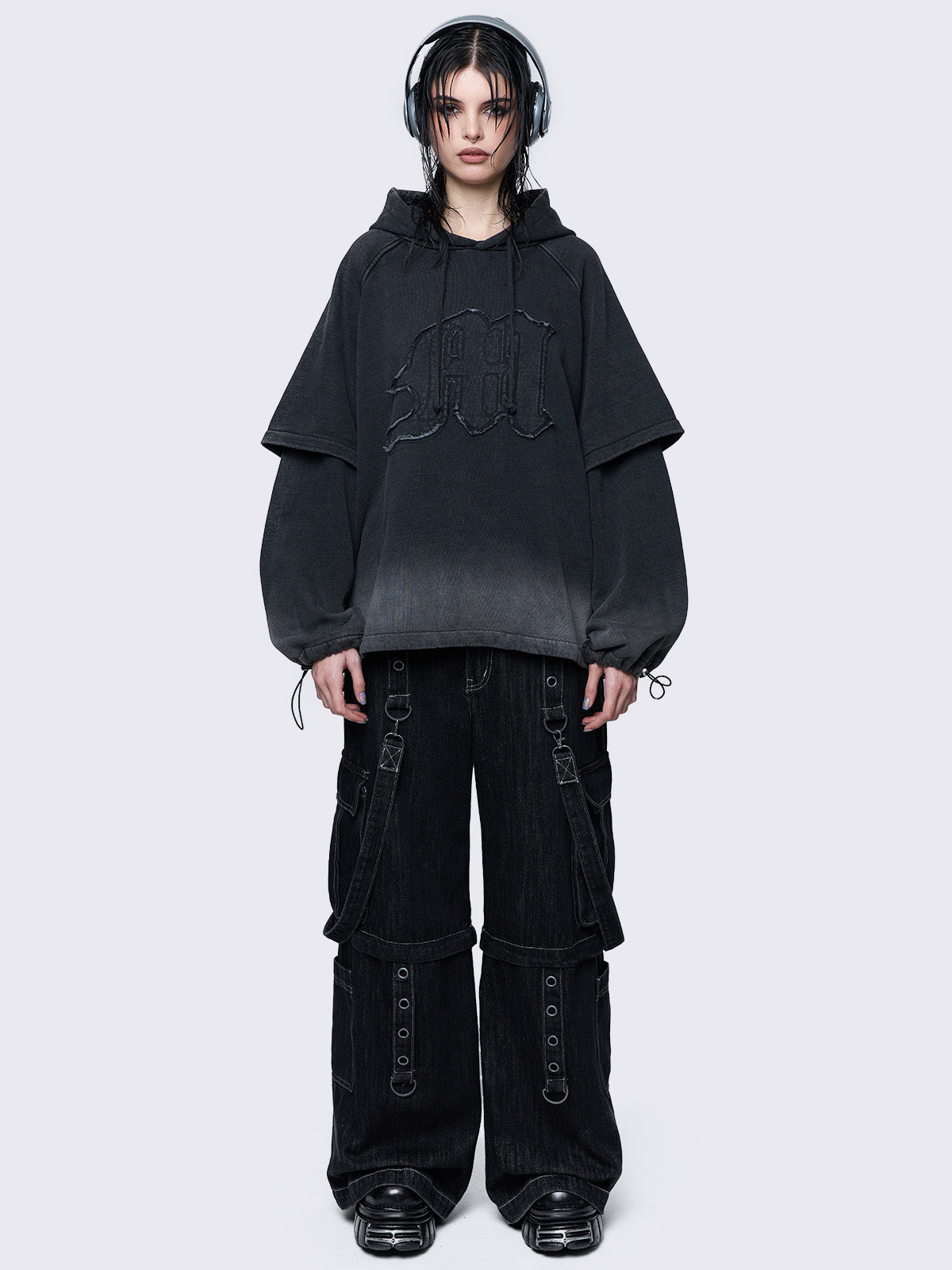 Oversized layered hoodie in washed black, featuring an embroidered "M" patch on the front, faded cuffs and hem, a drawstring hood, toggle elastic drawstrings, and raglan long sleeves.