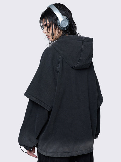 Oversized layered hoodie in washed black, featuring an embroidered "M" patch on the front, faded cuffs and hem, a drawstring hood, toggle elastic drawstrings, and raglan long sleeves.