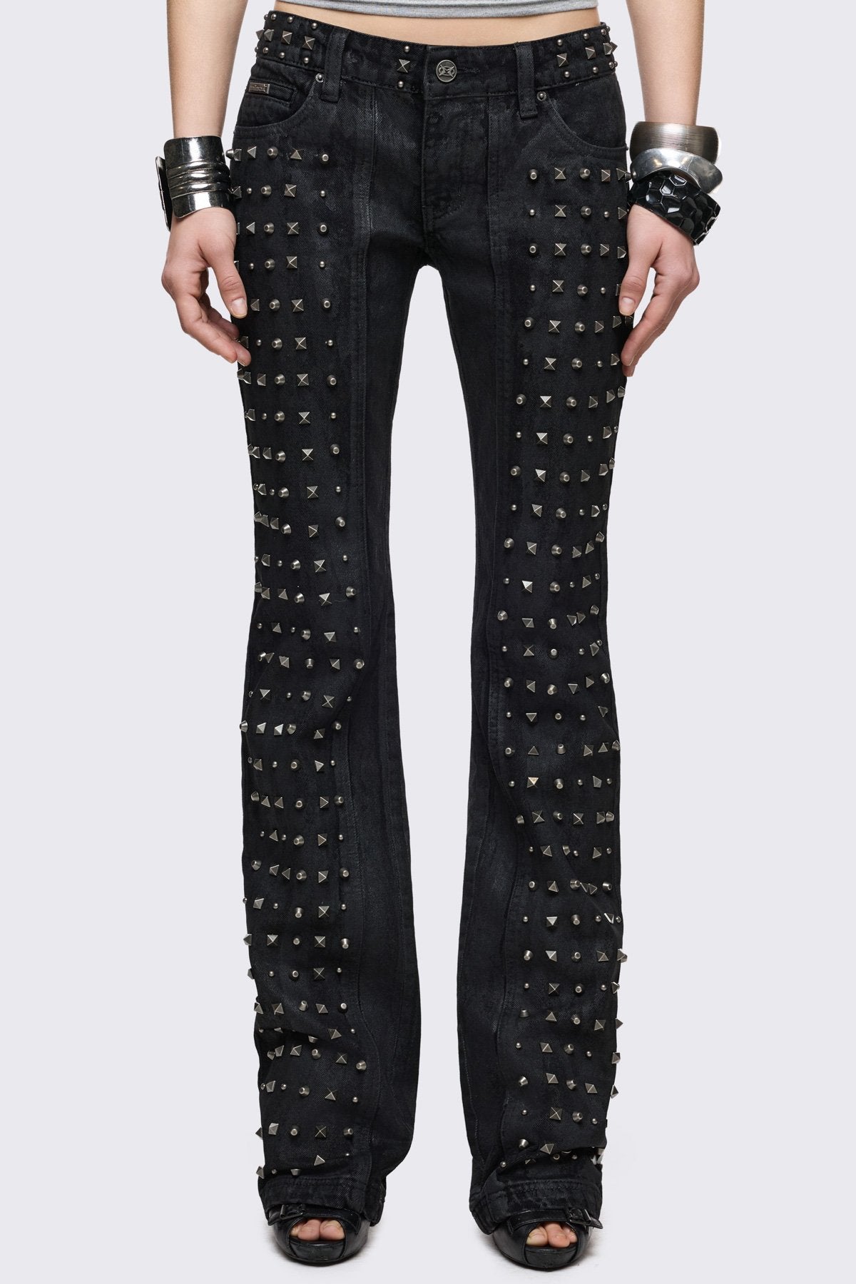 Black bootcut jeans in cotton blend with silver spikes and studded leg panels, low-rise grunge aesthetic.
