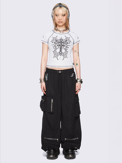 Black tech cargo parachute pants featuring multiple utility pockets with zipper and carabiner hardware detail - edgy, utility-inspired streetwear style.
