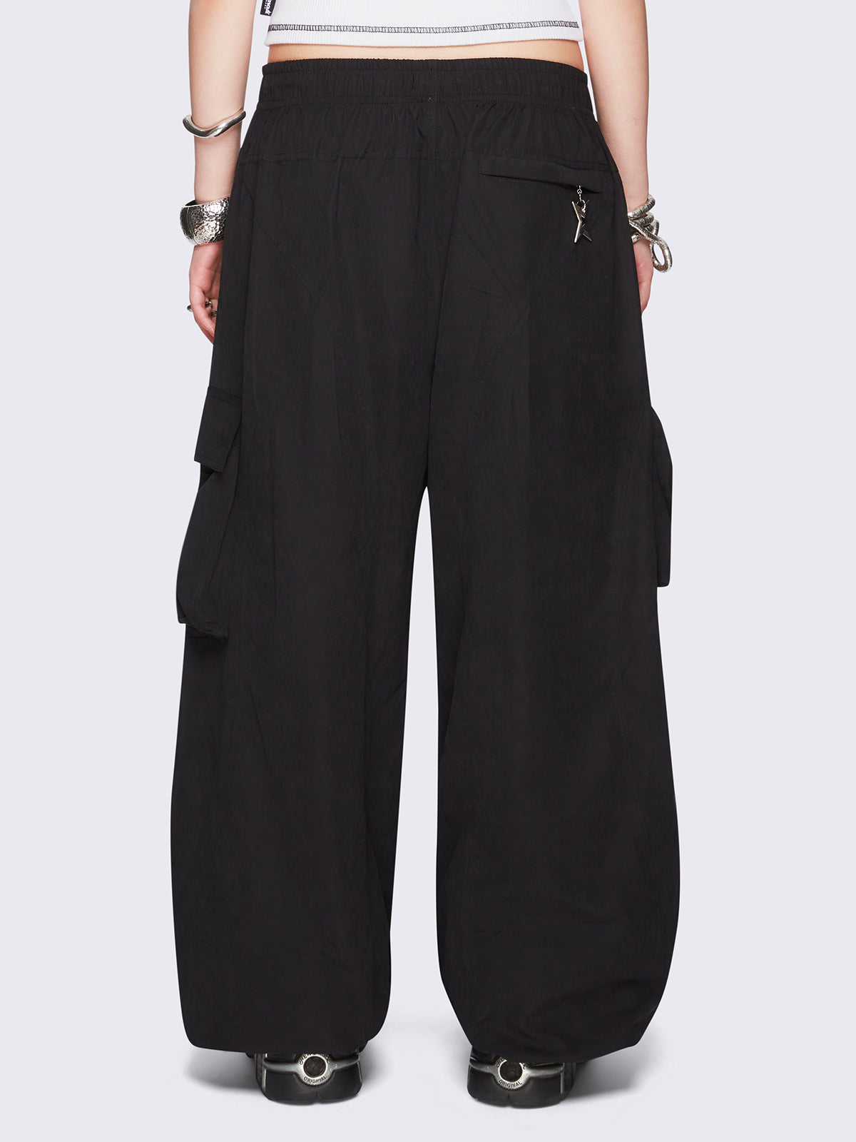 Black tech cargo parachute pants featuring multiple utility pockets with zipper and carabiner hardware detail - edgy, utility-inspired streetwear style.