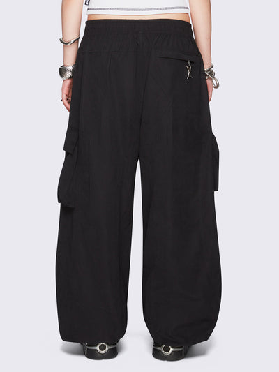 Black tech cargo parachute pants featuring multiple utility pockets with zipper and carabiner hardware detail - edgy, utility-inspired streetwear style.