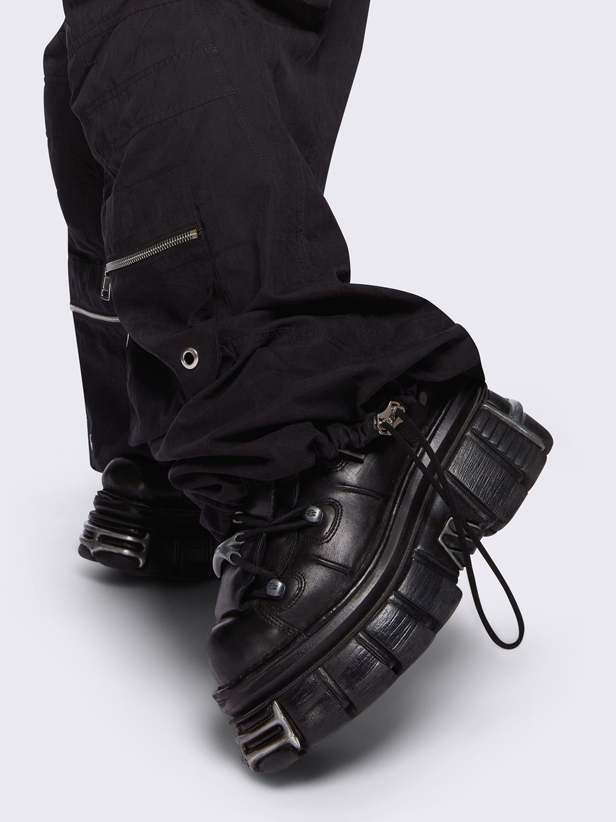 Black tech cargo parachute pants featuring multiple utility pockets with zipper and carabiner hardware detail - edgy, utility-inspired streetwear style.