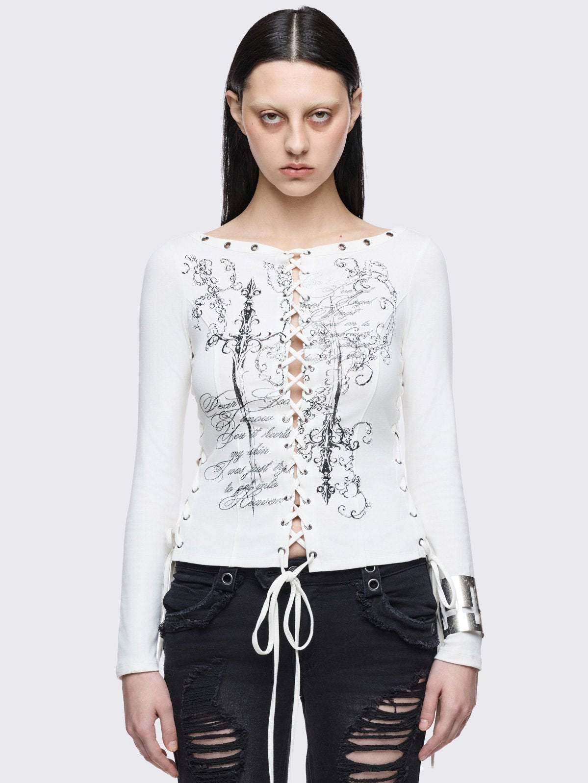 White long sleeve top with lace-up corset on front and sleeves featuring a daggers graphic front print