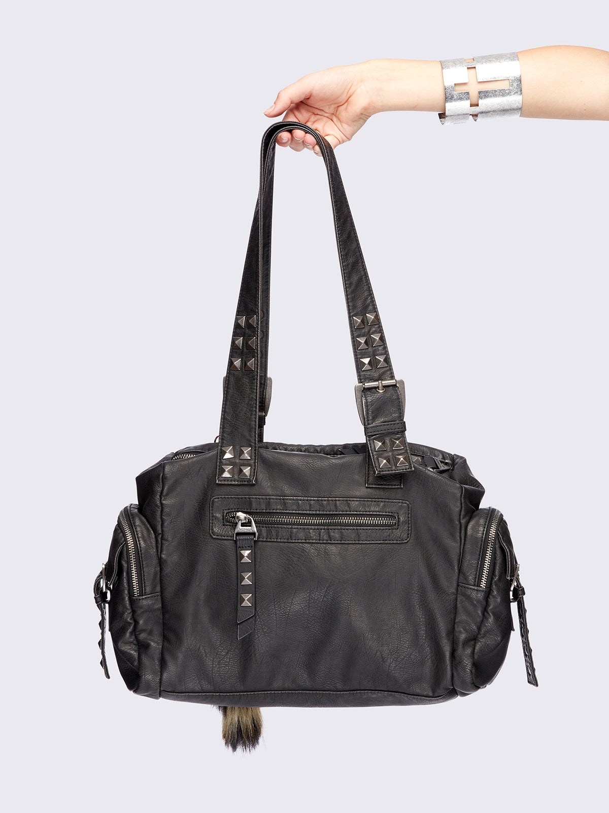 Black faux leather shoulder bag with pyramid studs, metal hardware details and removable faux fur fox tail keychain.